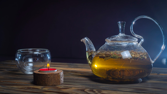 Glass teapot with herbal infusion beside a small candle in Danish hygge style